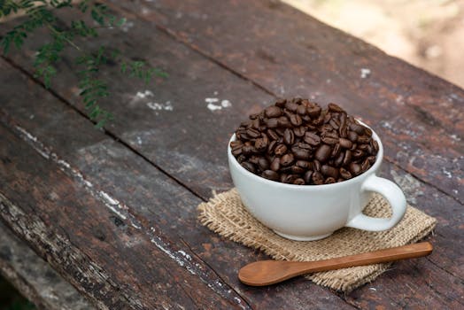 A white mug filled with roasted coffee beans on a rustic wooden table outdoors.
